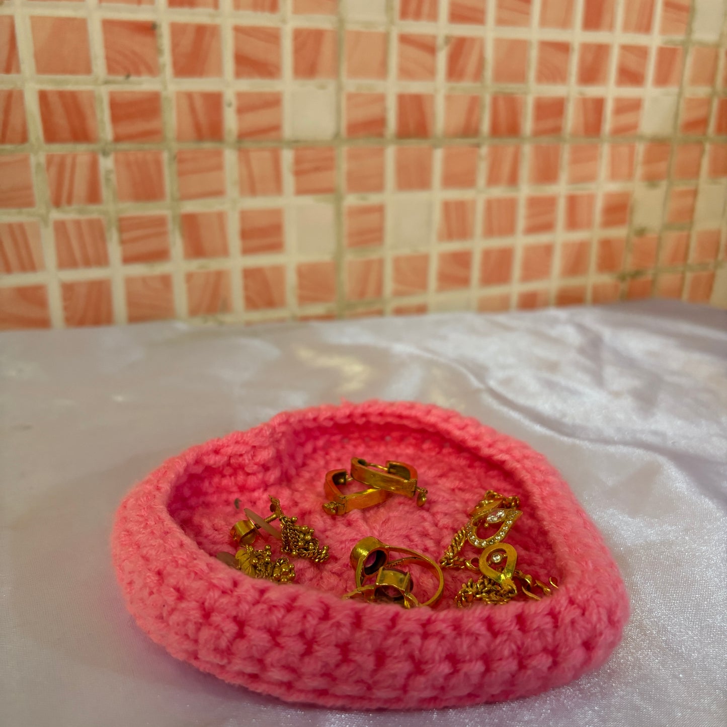 Pink crocheted dish with gold earrings on a white surface with pink tiled wall background