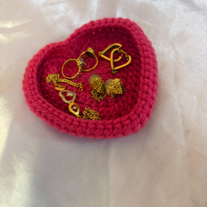 Heart-shaped pink crochet dish with gold jewelry on a white background