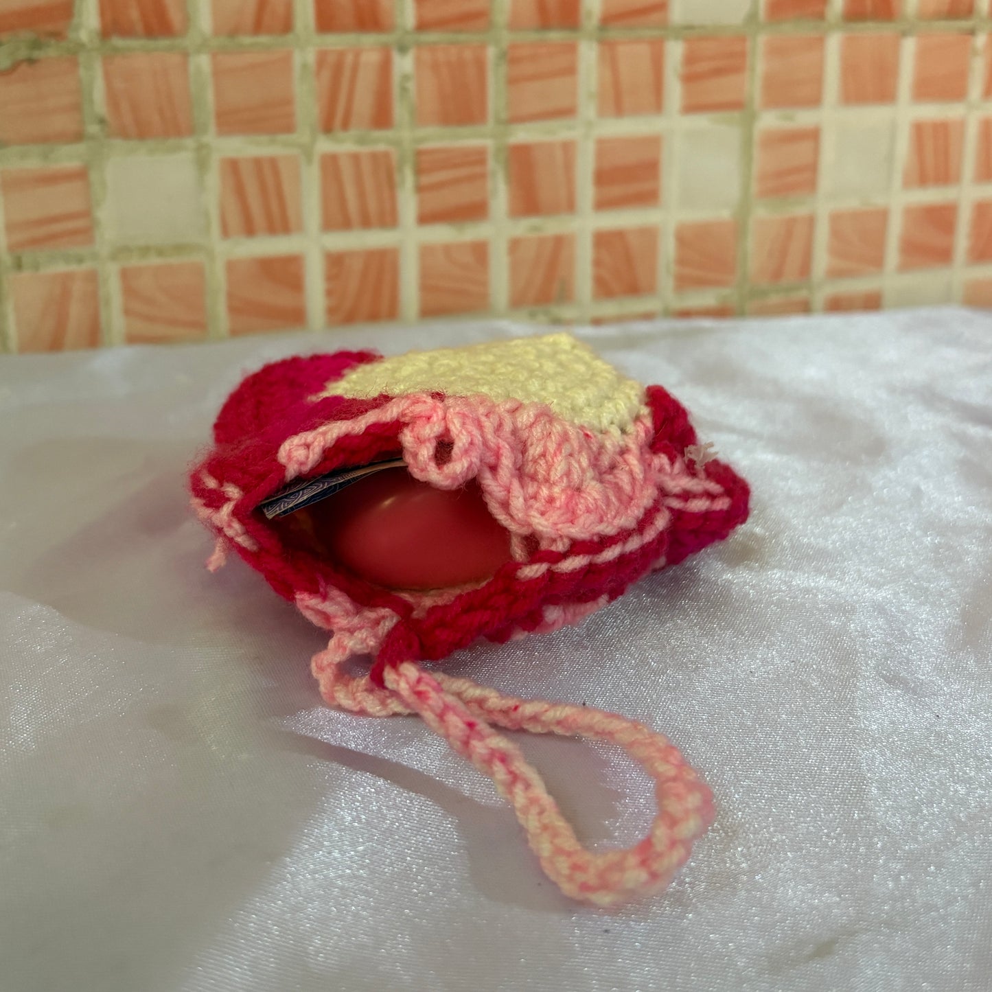 crochet pouch with a earphones and cash on a textured surface with a tiled wall background