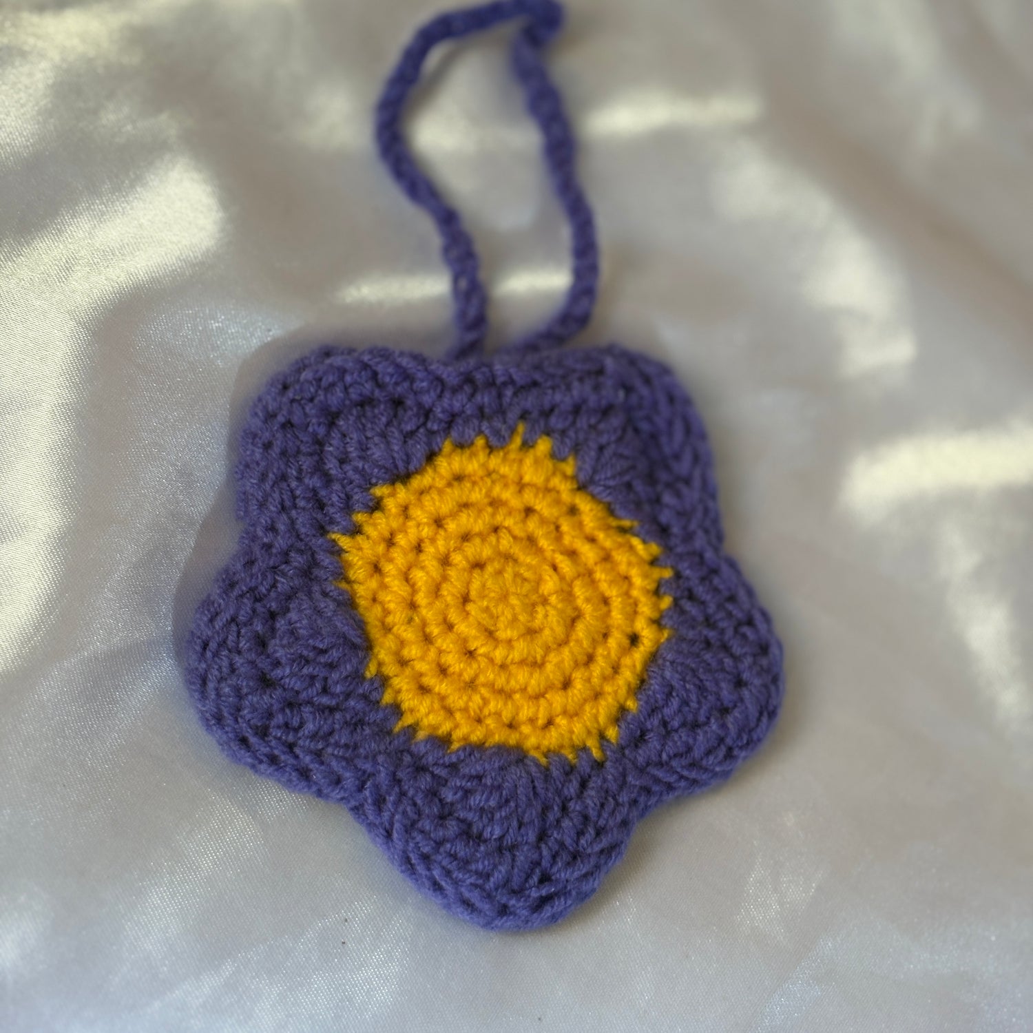 Crocheted flower pouchwith purple petals and yellow center on a white background