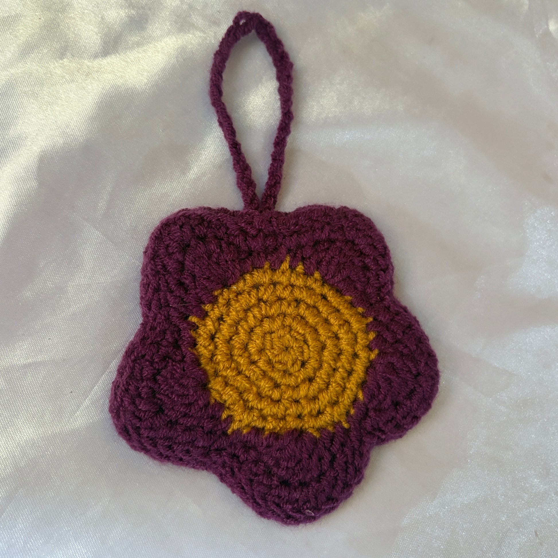 Crocheted flower pouch with purple petals and yellow center on a white fabric background