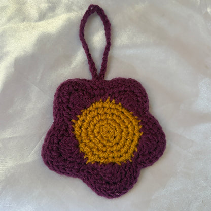 Crocheted flower pouch with purple petals and yellow center on a white fabric background