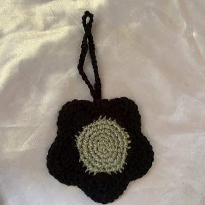 Crocheted black and green flower-shaped pouch on a light fabric background