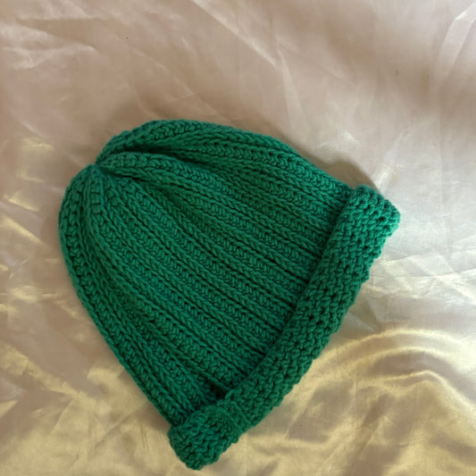 Green crochet beanie on a light beige fabric background