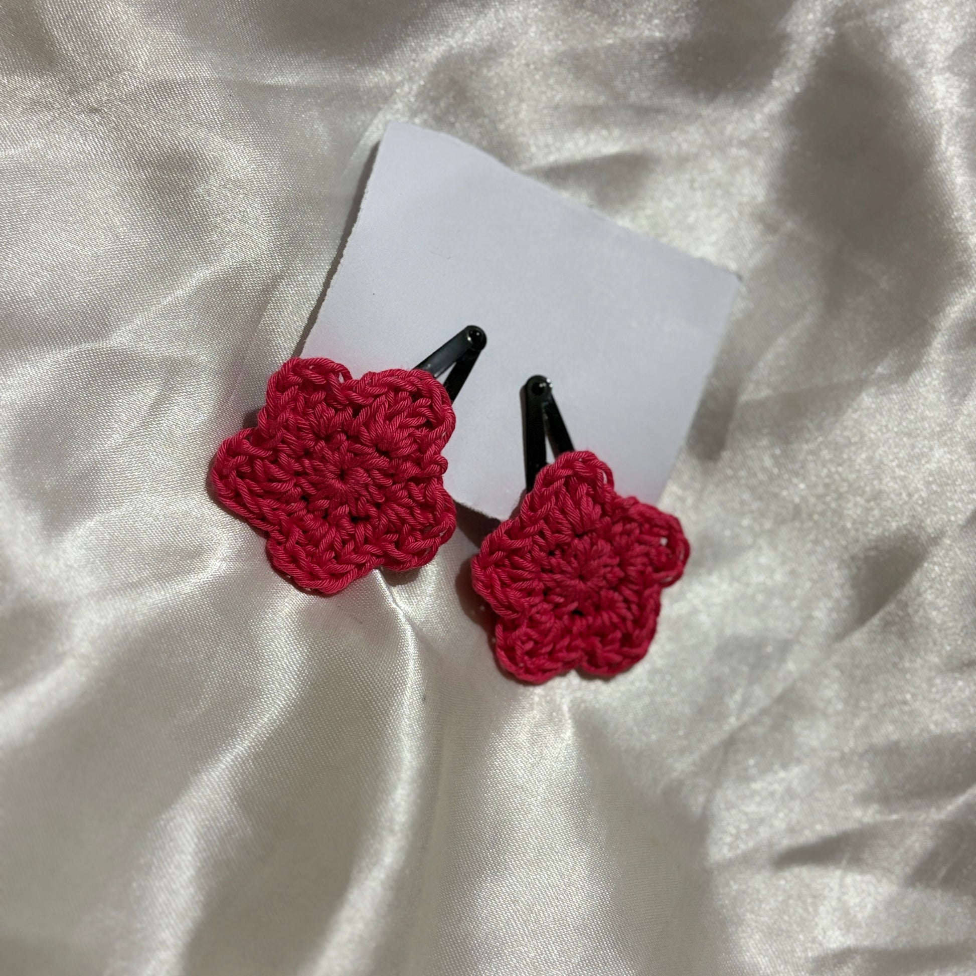 Red crocheted hair clips on a white card with a white fabric background