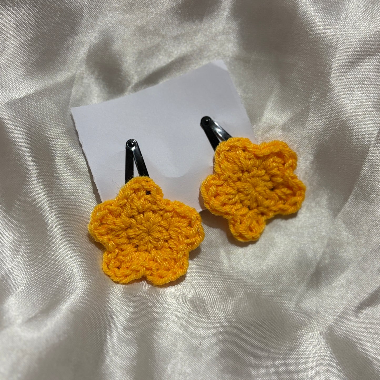 Yellow crocheted hair clips on a white fabric background