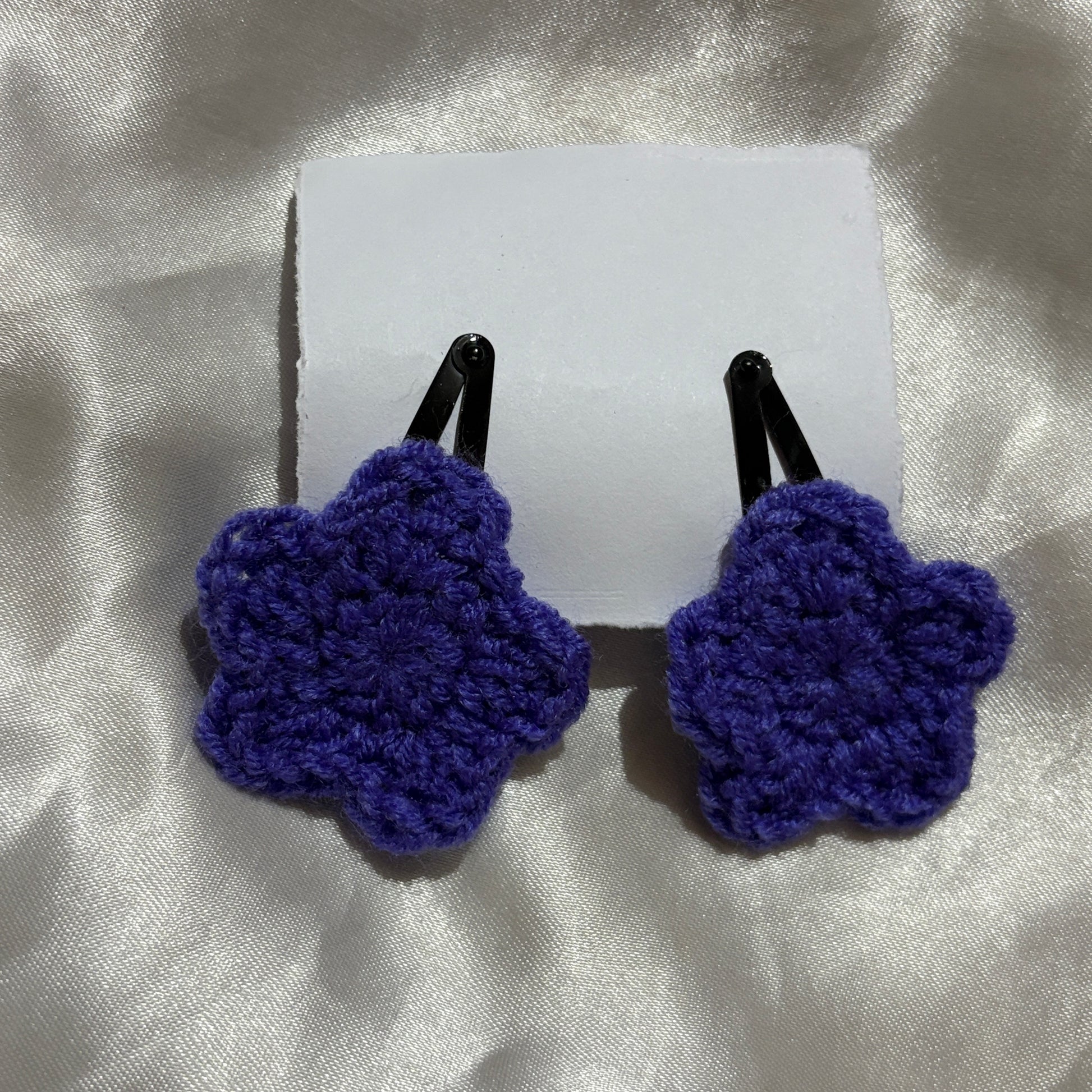 Pair of blue crocheted hair clips on a white card with a silver background