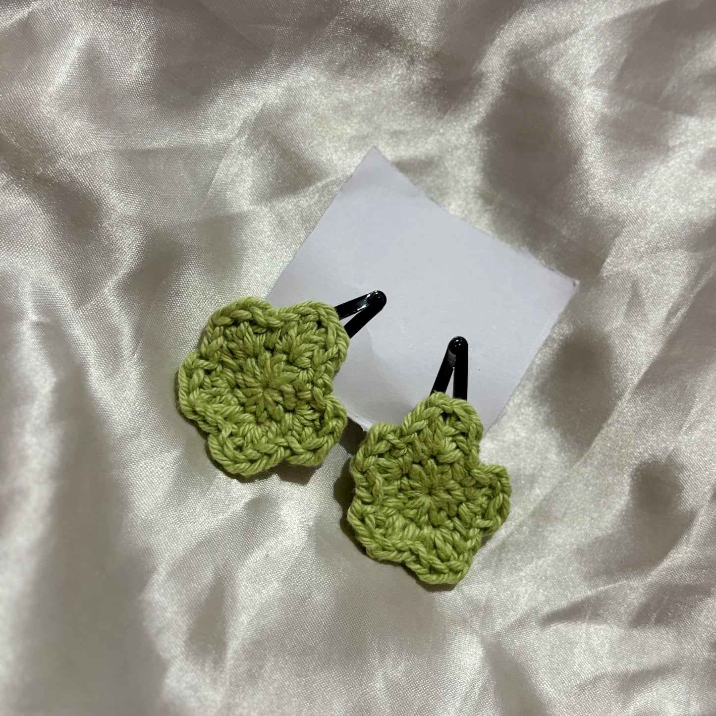 Green crocheted hair clips on a white fabric background