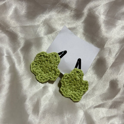 Green crocheted hair clips on a white fabric background