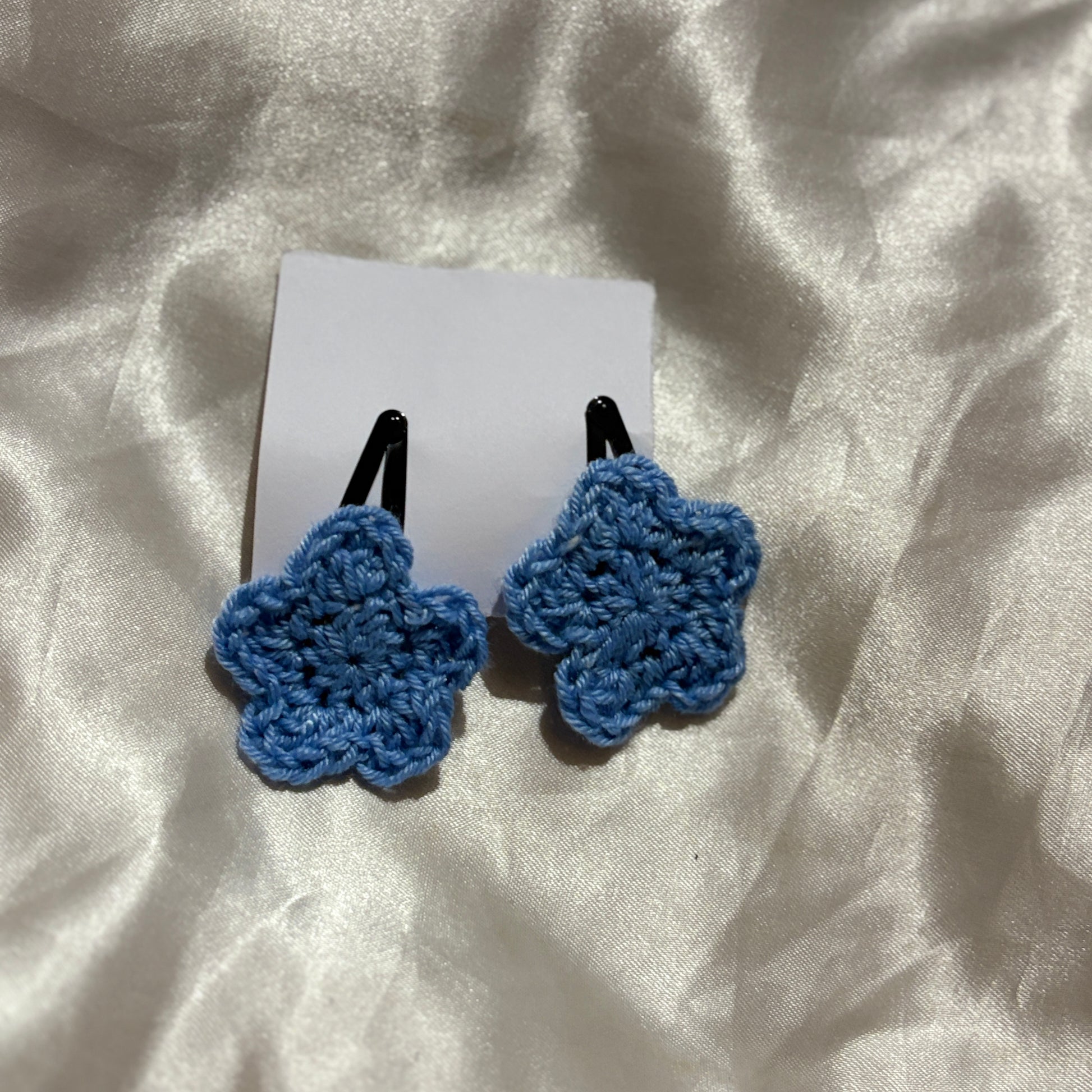 Blue crocheted hair clips on a white card with a white fabric background