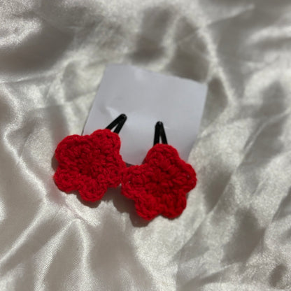 Red crocheted hair clips on a white fabric background