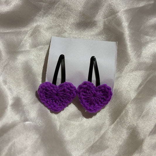 Purple heart-shaped hair clips on a white card with a white fabric background