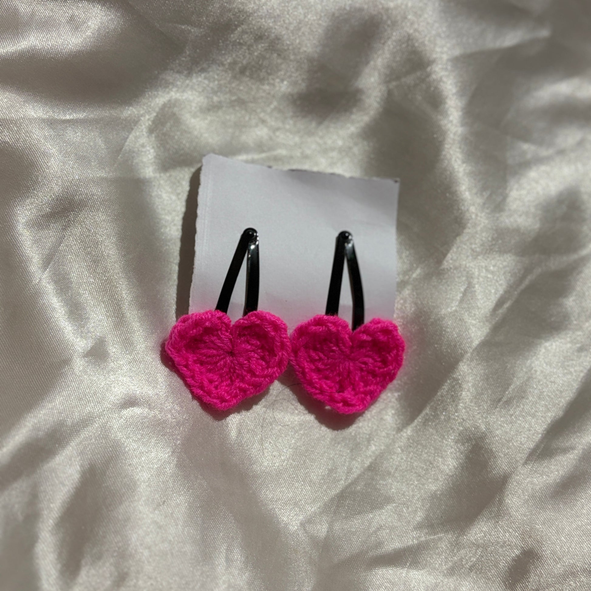 Pink heart-shaped earrings on a white card with a white fabric background