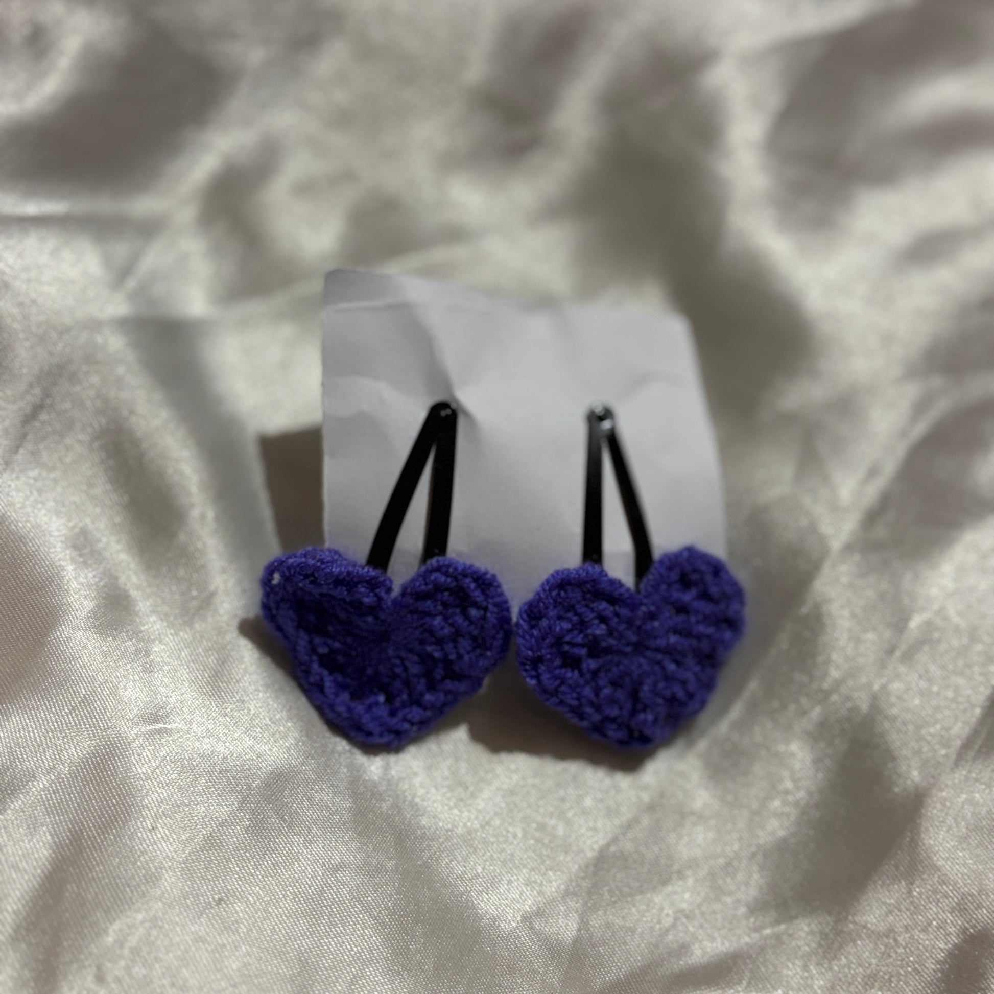 Pair of blue heart-shaped hair clips on a white card with a textured beige background