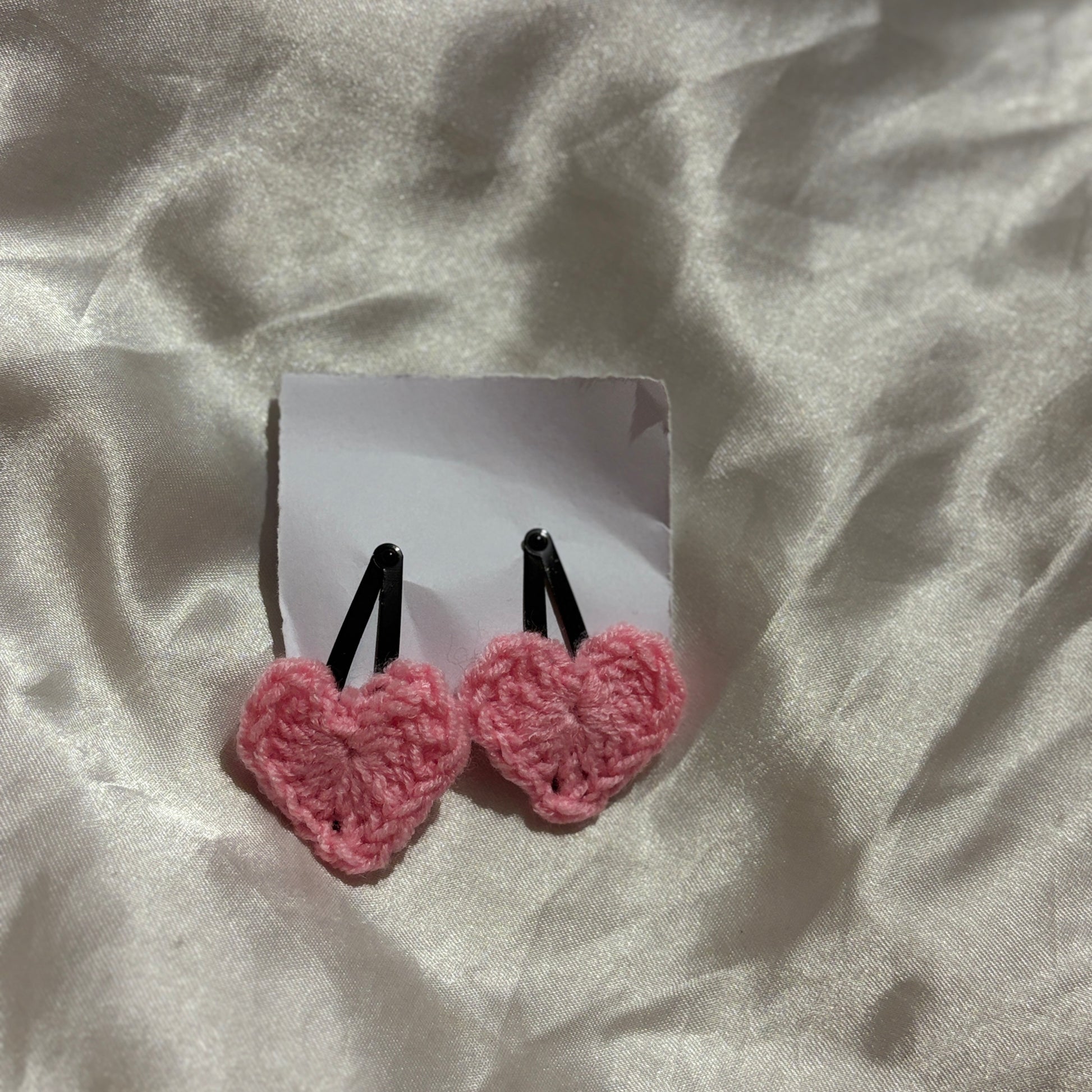 Pink heart-shaped earrings on a white card against a textured beige background