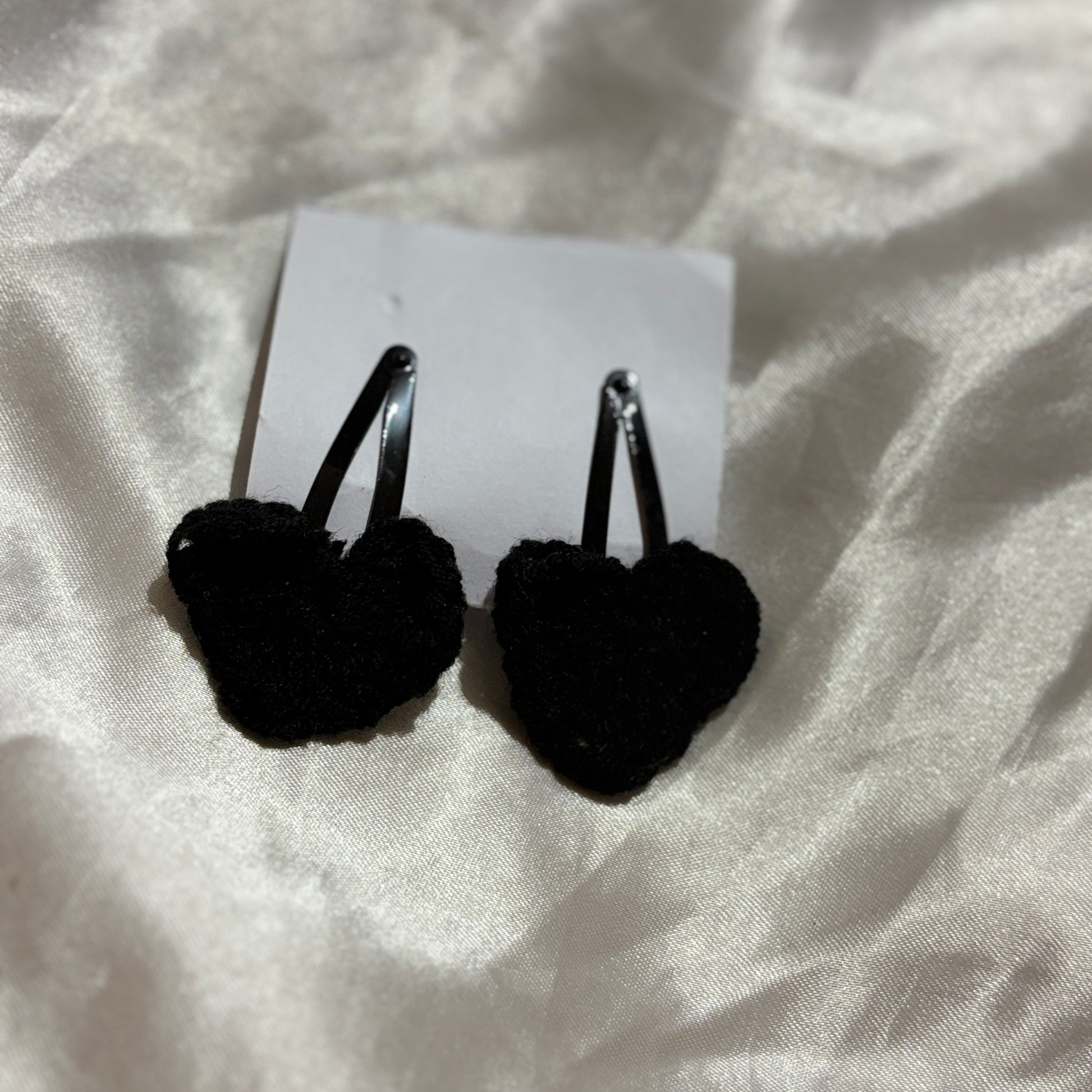Black heart-shaped earrings on a white card with a white fabric background