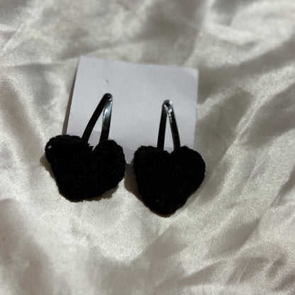 Black heart-shaped earrings on a white card with a white fabric background
