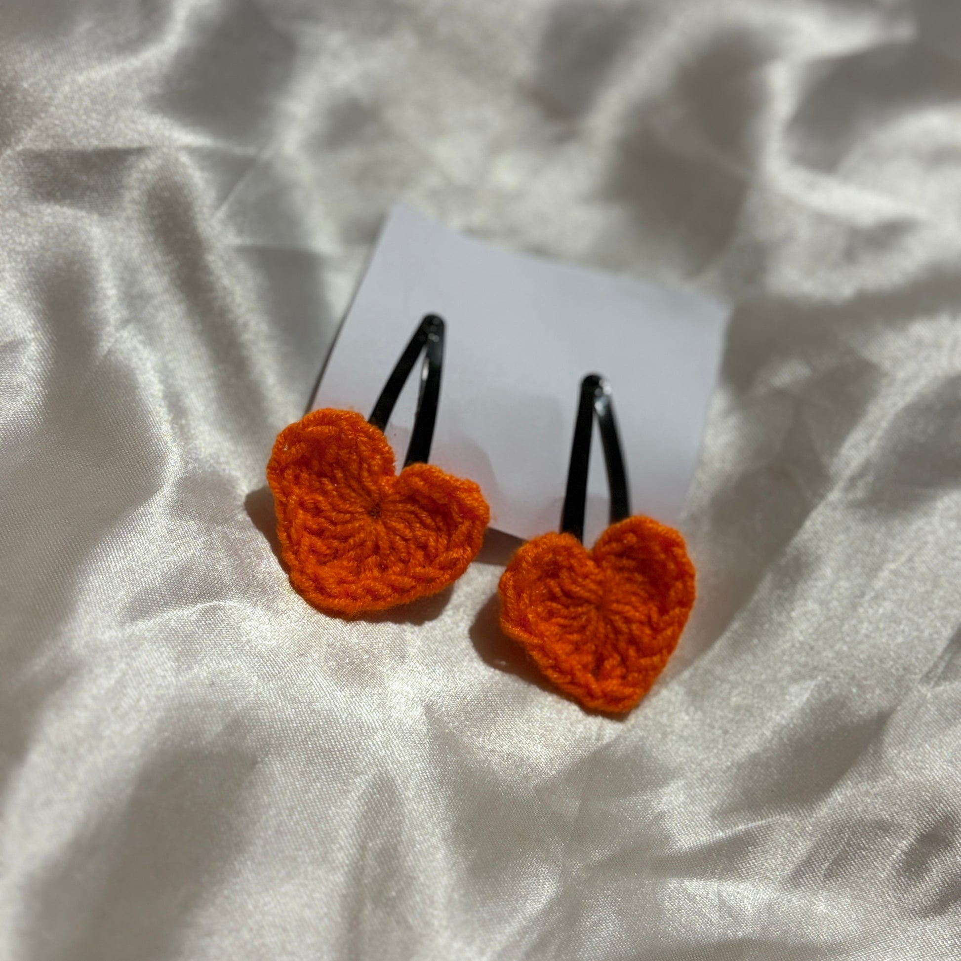 Orange heart-shaped crocheted clips on a white card with a white fabric background
