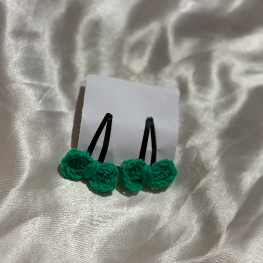 Green crocheted hair clips on a white card with a textured gray background