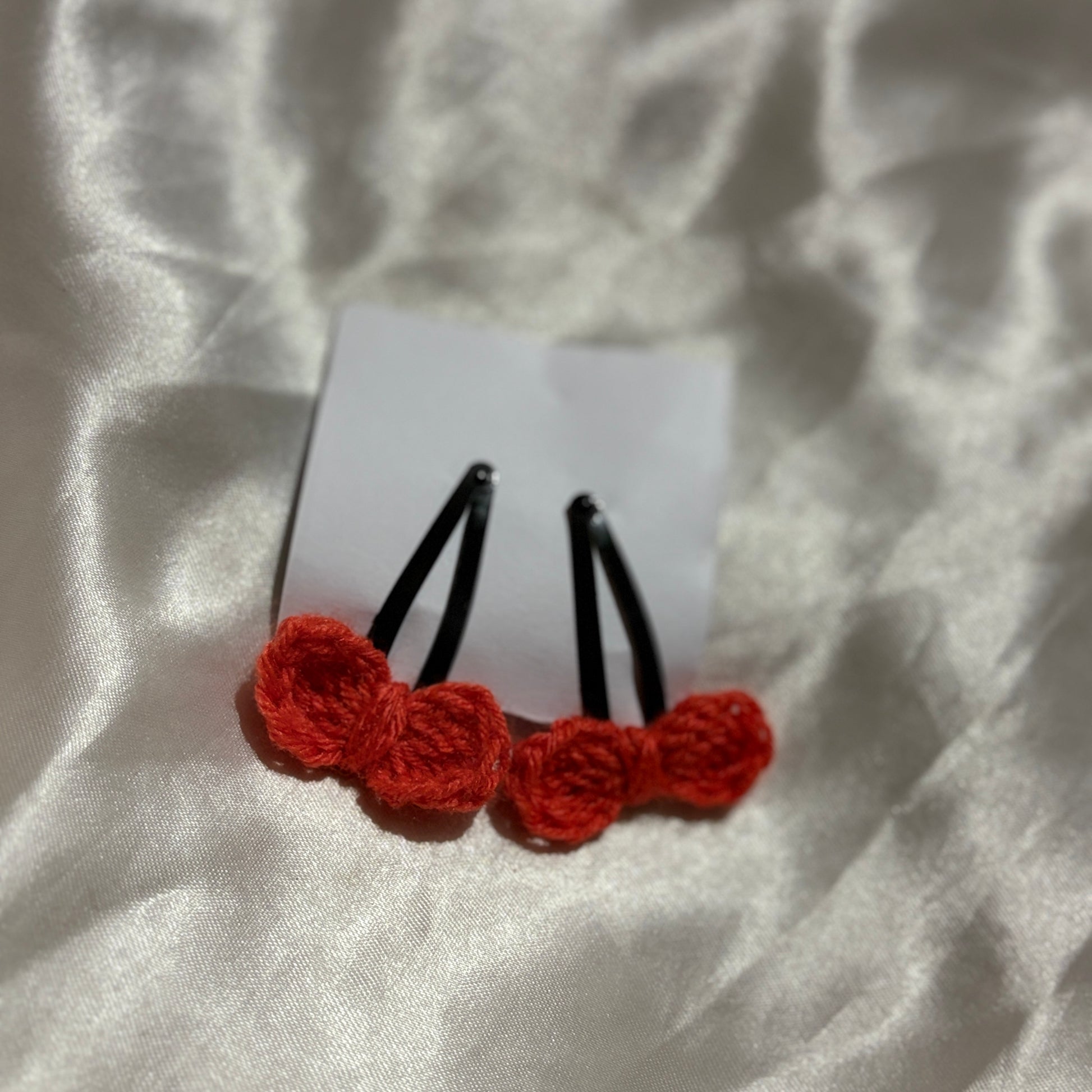 Red crocheted hair clips on a white fabric background