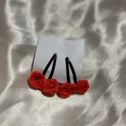 Red crocheted hair clips on a white fabric background
