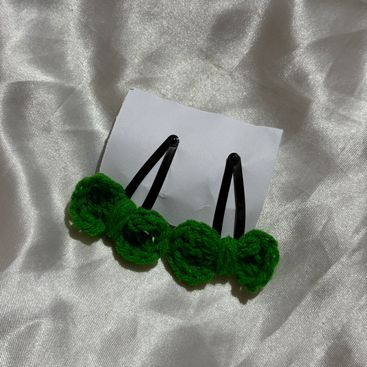 Two green crocheted hairpins on a white card with a silver fabric background