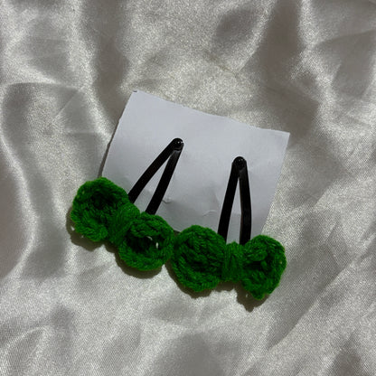 Two green crocheted hairpins on a white card with a silver fabric background