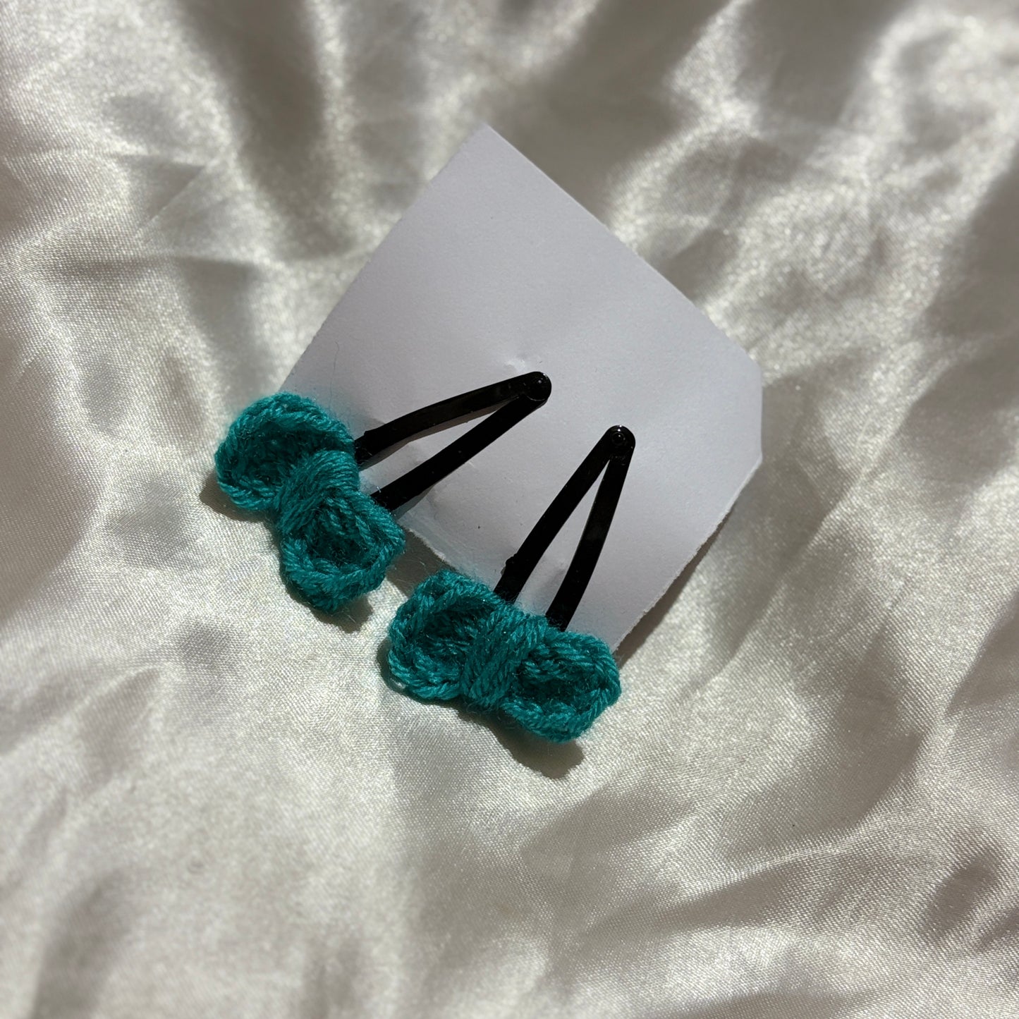 Two teal hair ties on a white card with a white fabric background