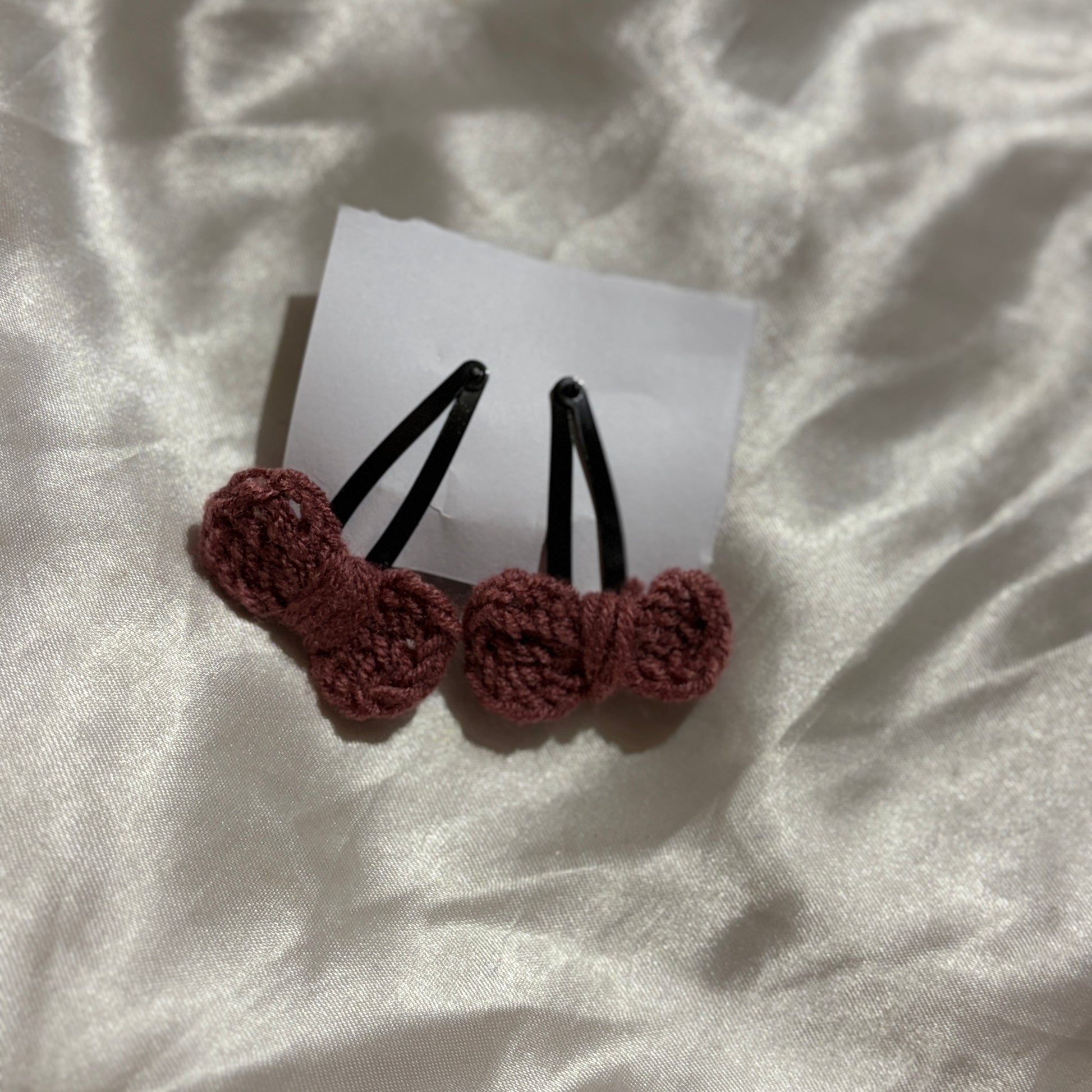 Two brown crochet hair clips on a white card with a white fabric background