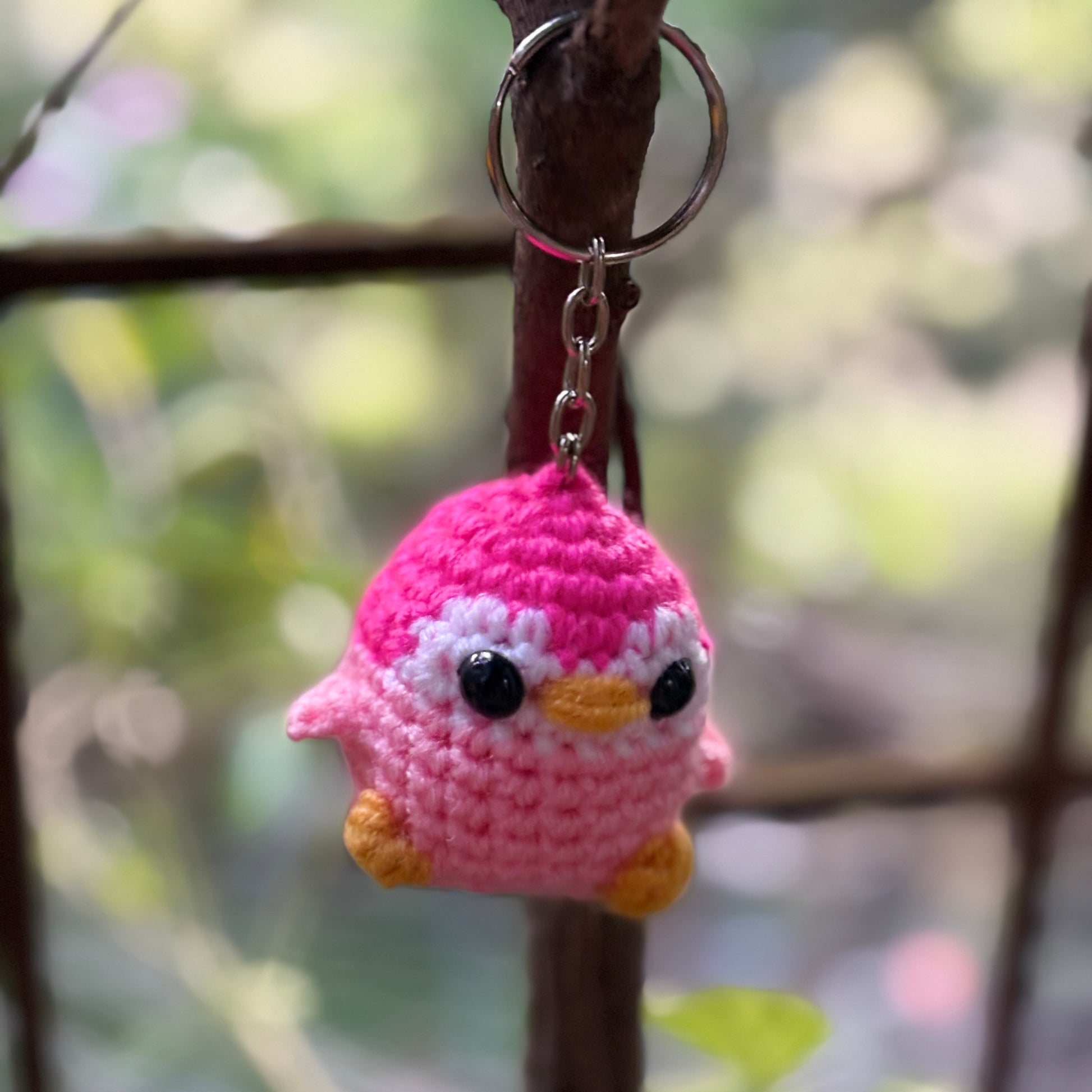 Crocheted penguin keychain hanging on a branch with a blurred natural background