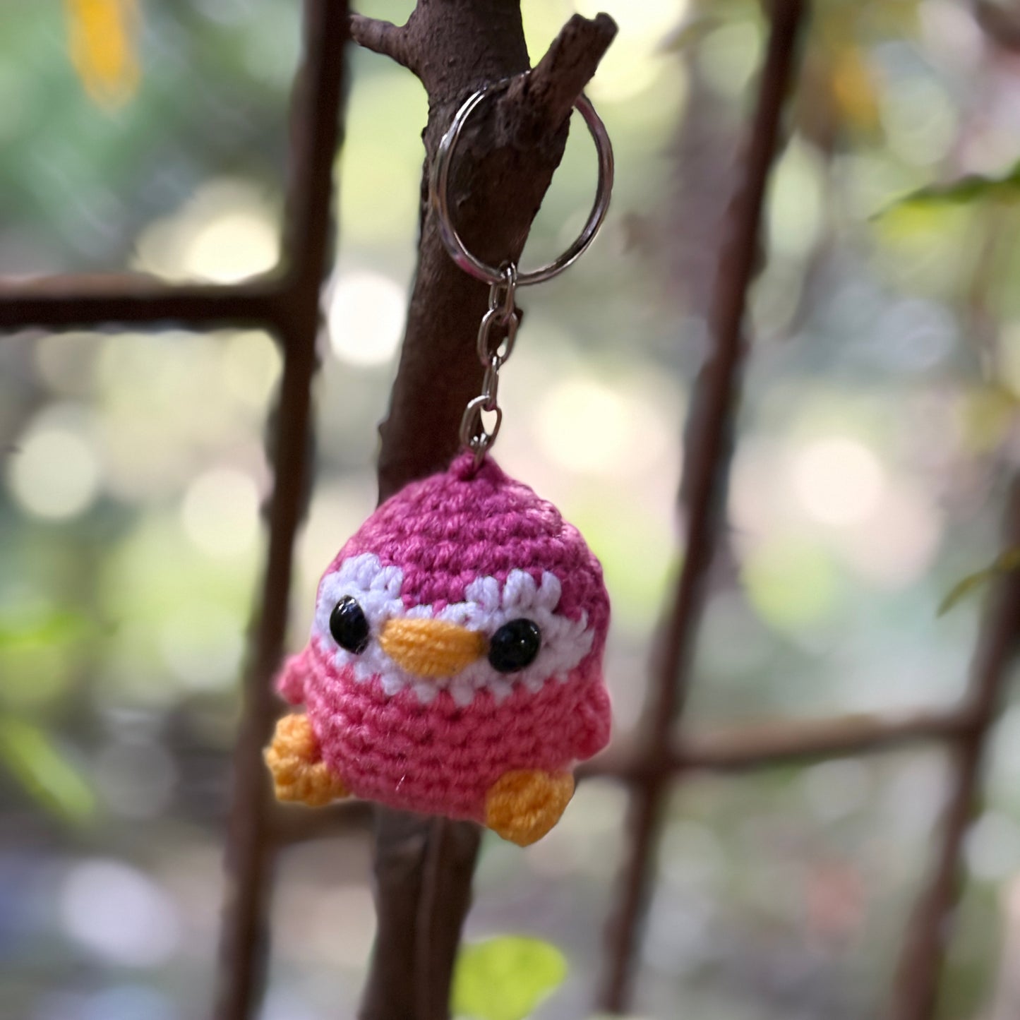 Crocheted penguin keychain hanging on a branch with a blurred natural background