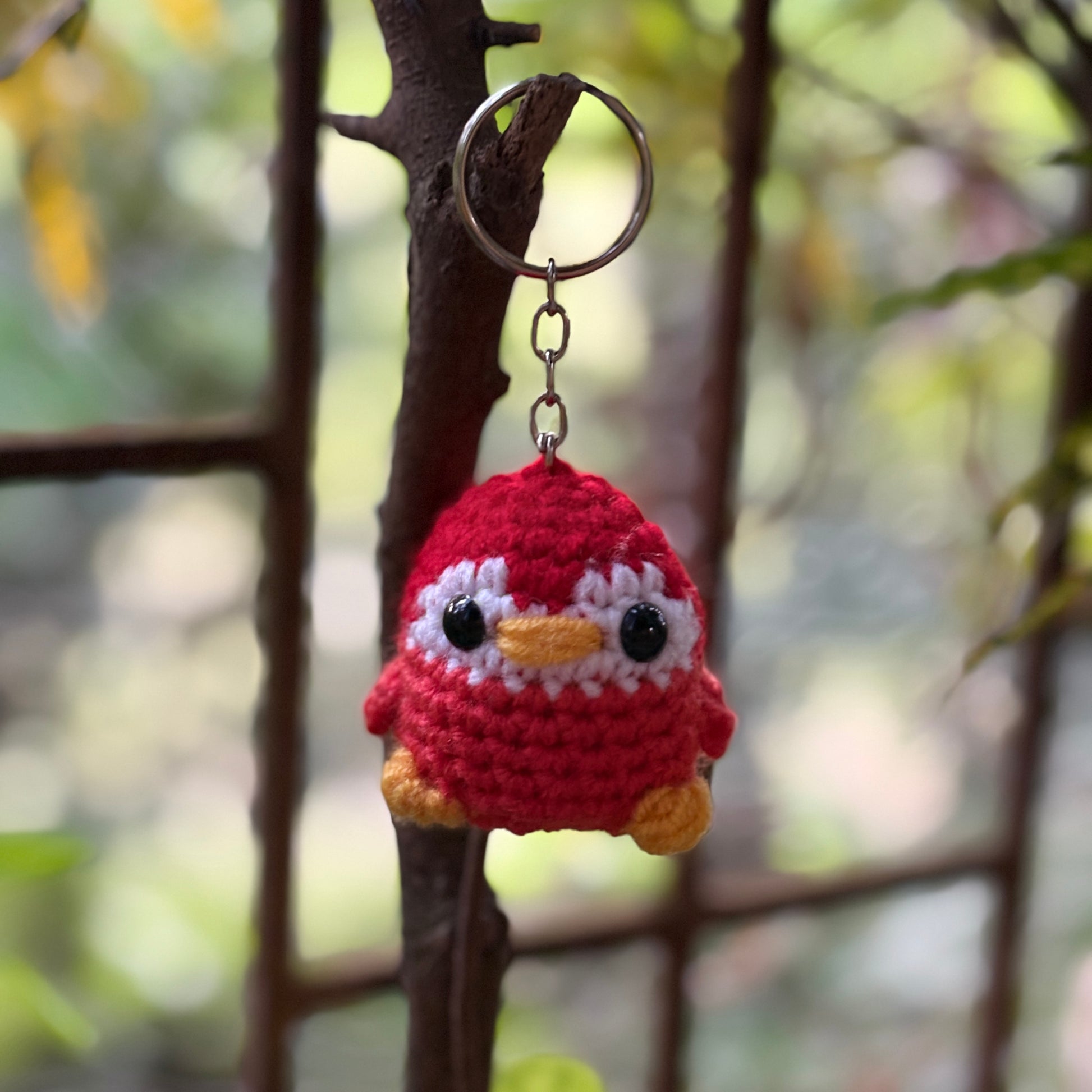Crocheted penguin keychain hanging on a branch with a blurred natural background