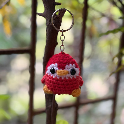 Crocheted penguin keychain hanging on a branch with a blurred natural background