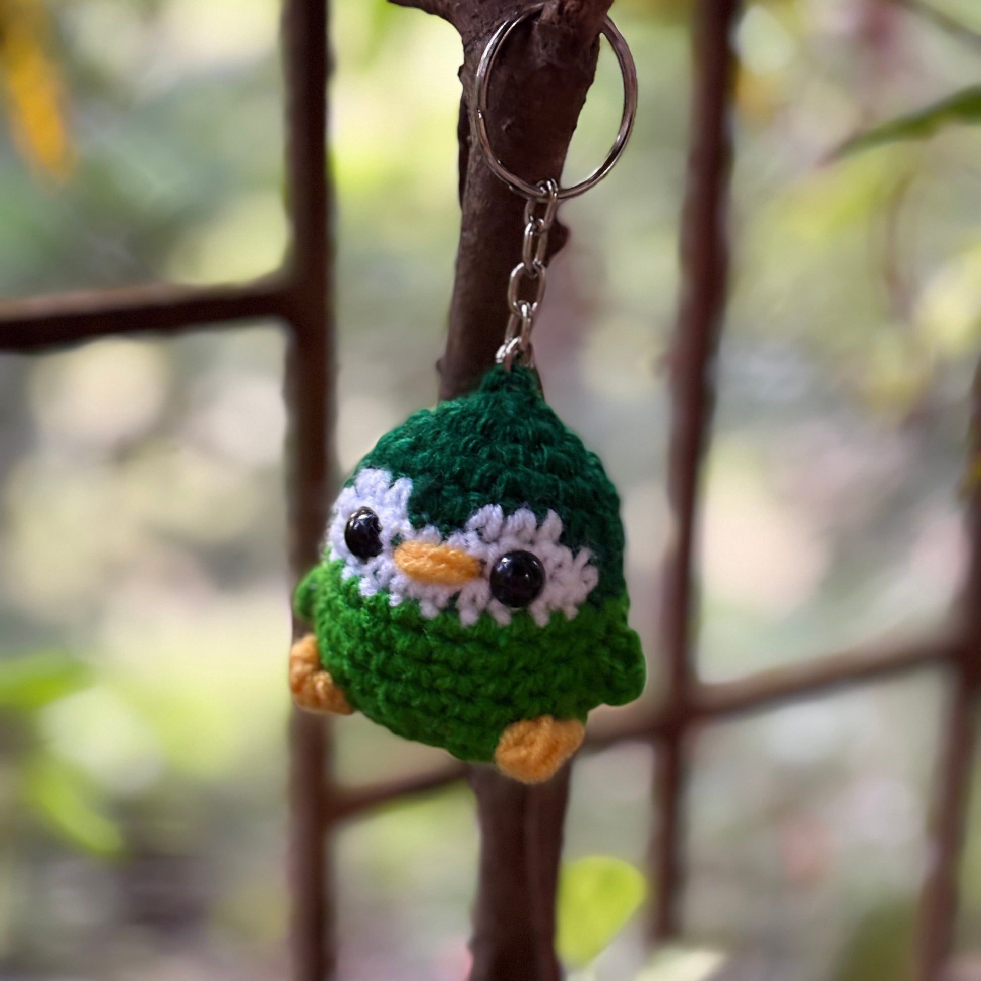 Crocheted penguin keychain hanging on a branch with a blurred natural background