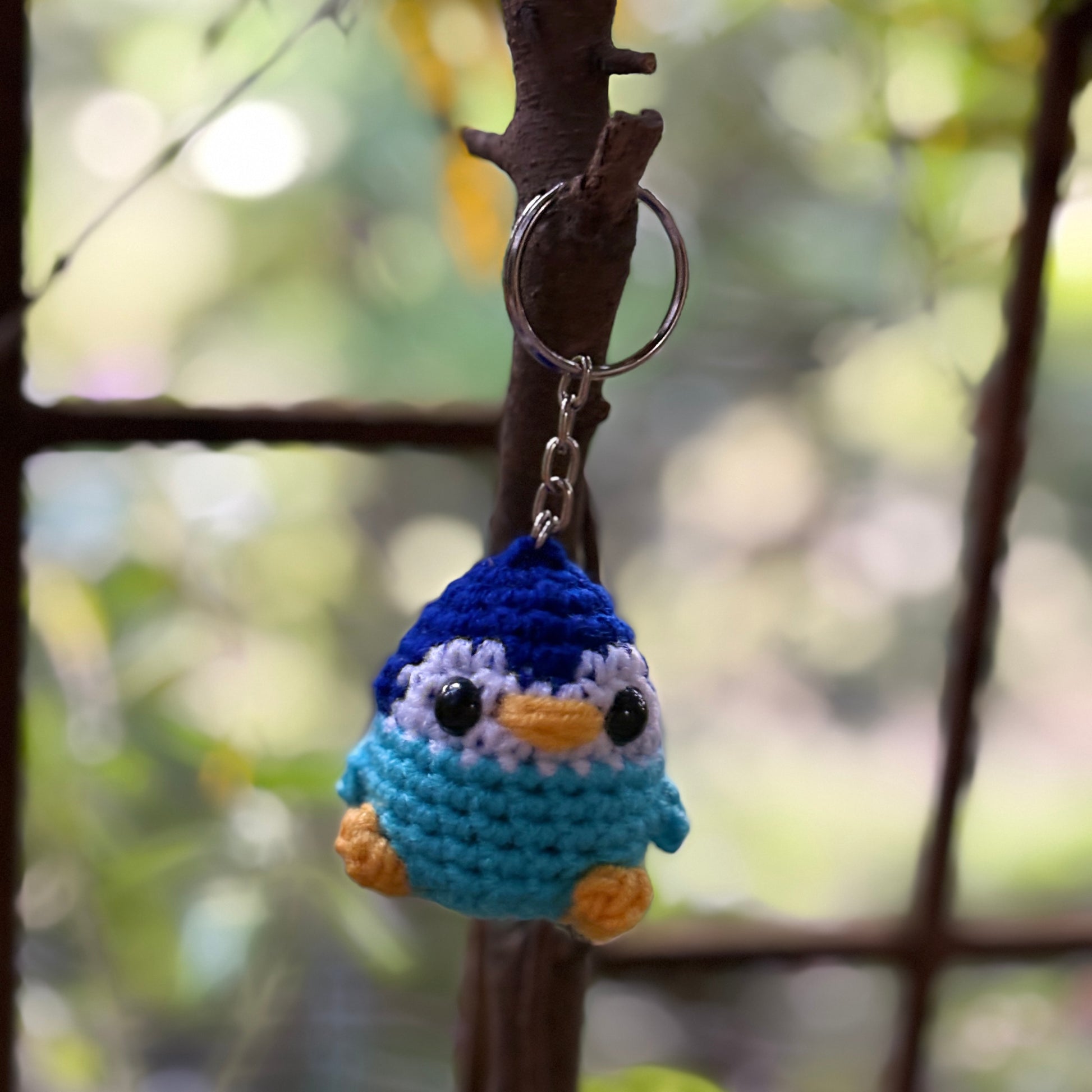 Crocheted penguin keychain hanging on a branch with a blurred natural background