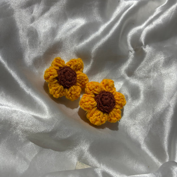 Two yellow crocheted sunflower clips on a white fabric background