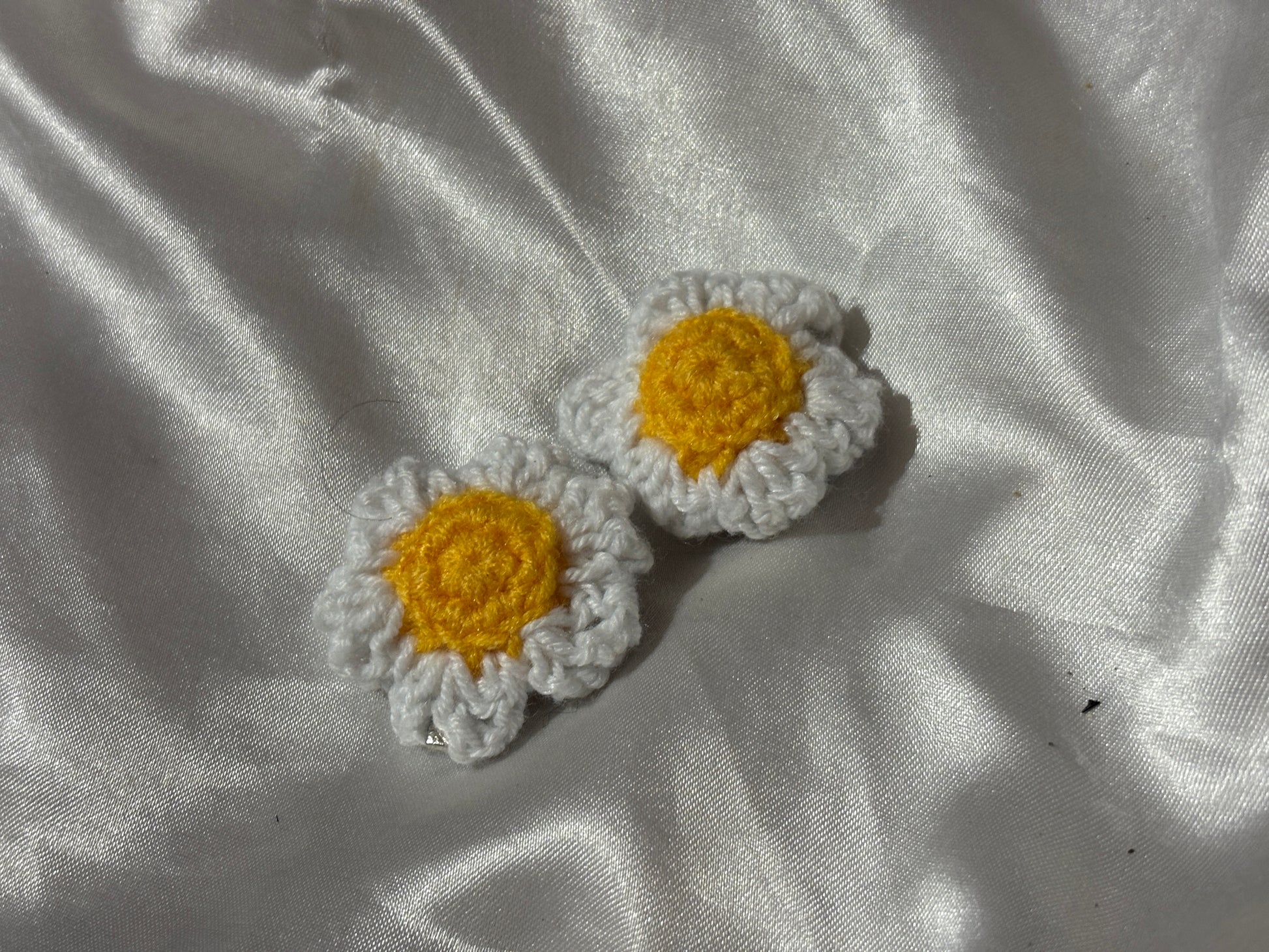 Two crocheted flower clips on a textured white fabric background