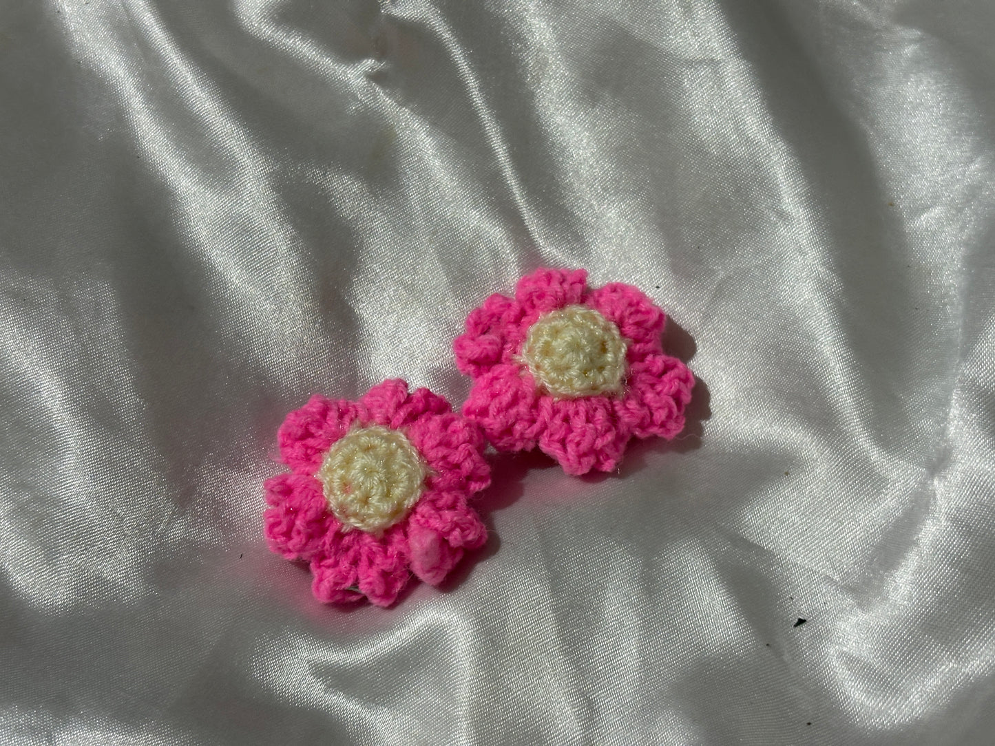 Two pink crocheted flower-shaped clips on a white fabric background