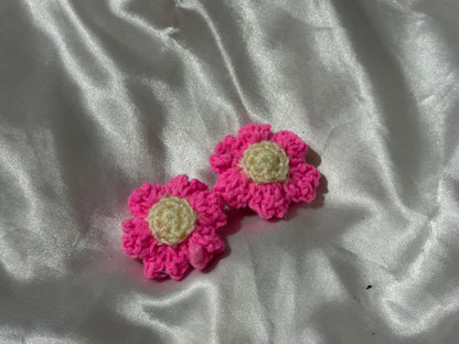 Two pink crocheted flower-shaped clips on a white fabric background