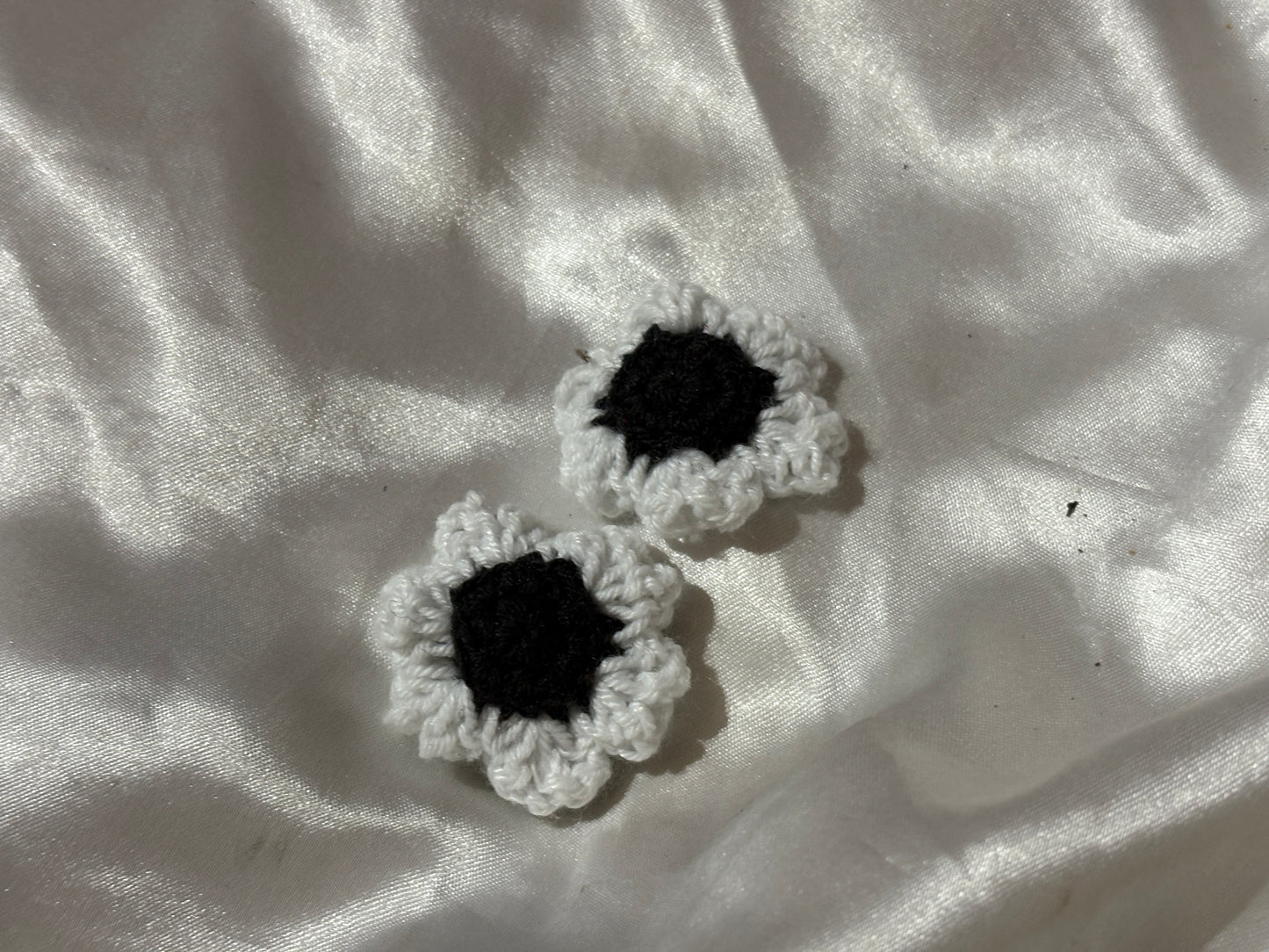 Two black and white crocheted flower clips on a textured white fabric background
