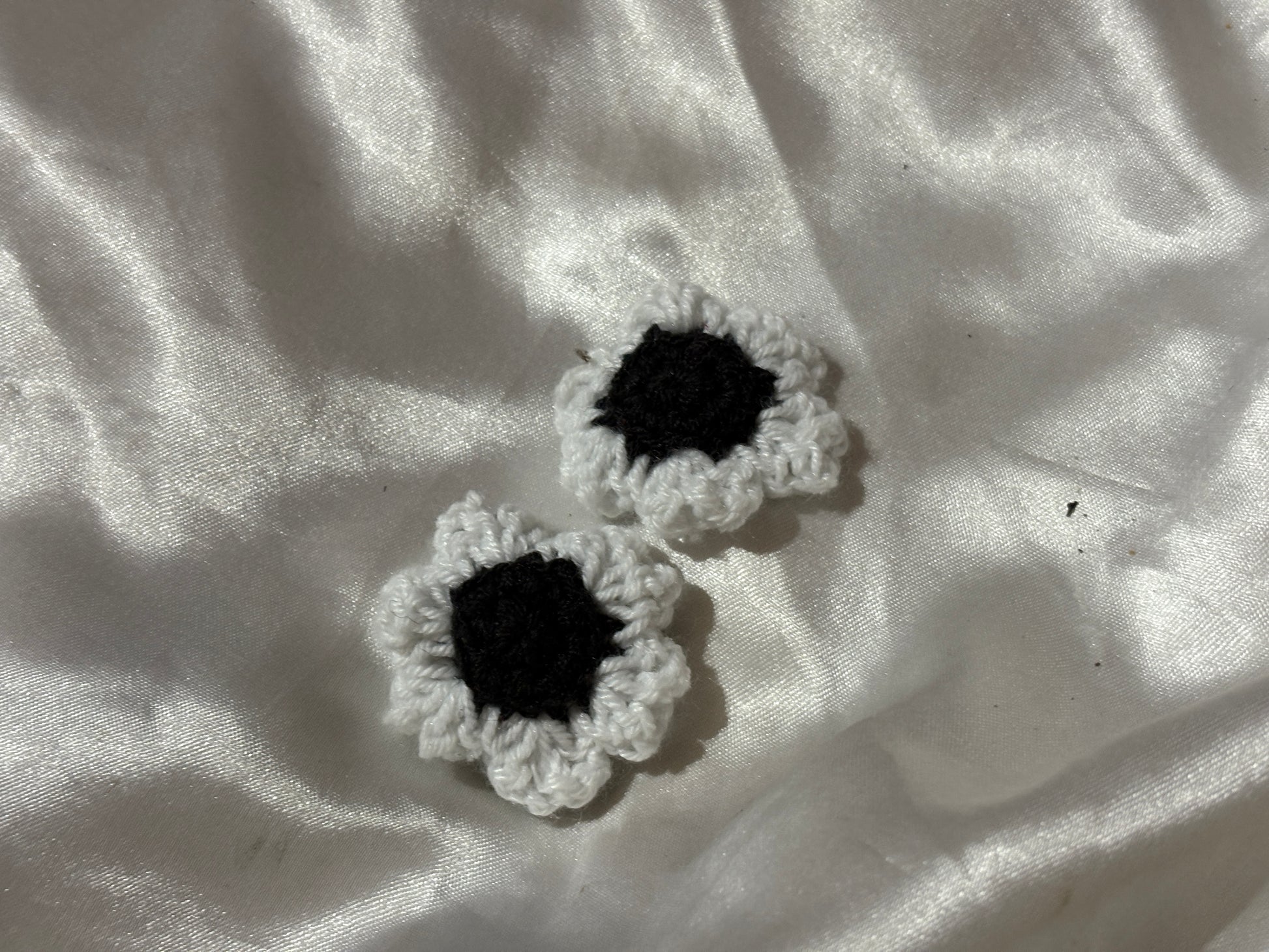 Two black and white crocheted flower clips on a textured white fabric background
