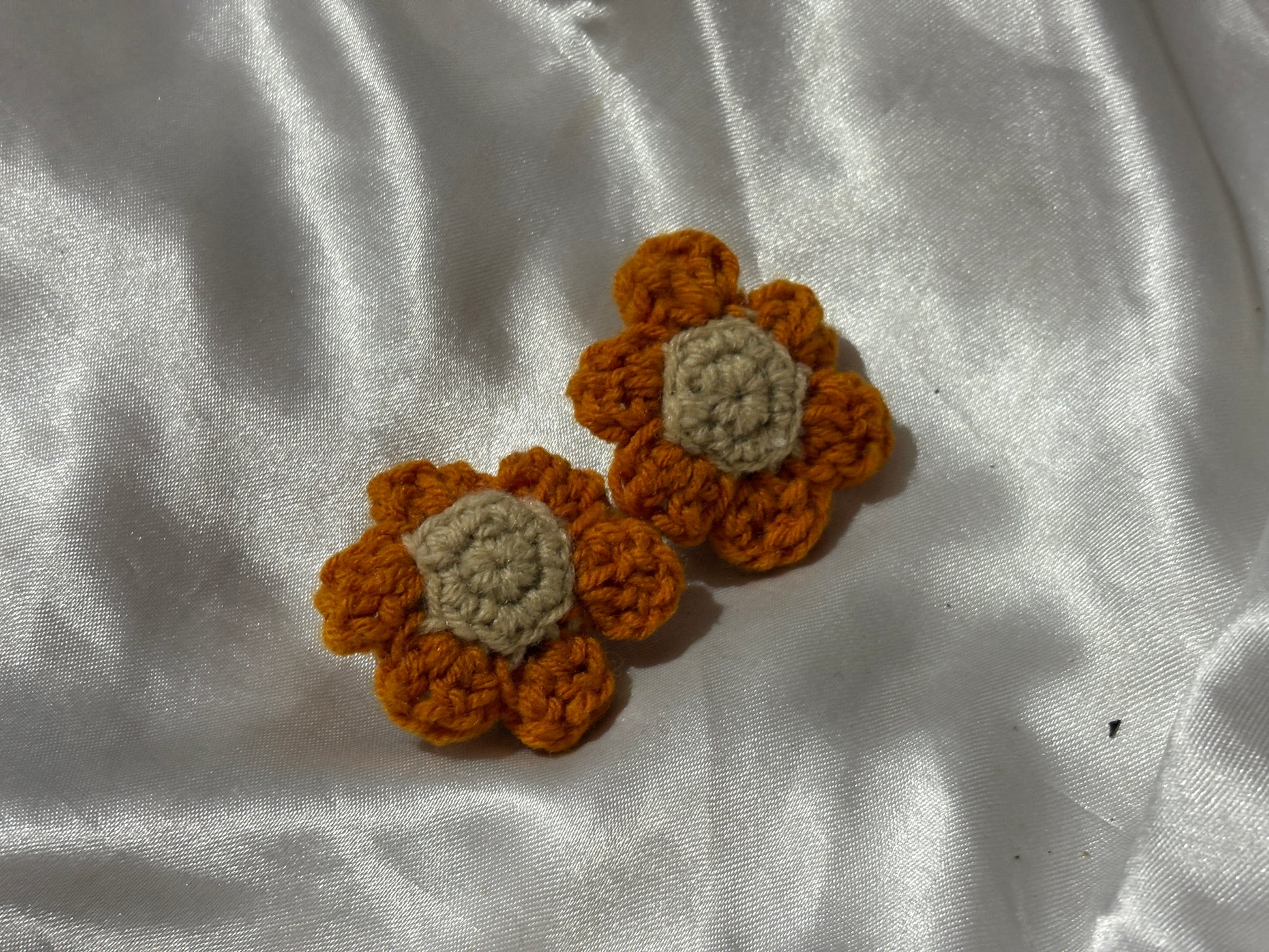 Two crocheted flower clips on a white fabric background