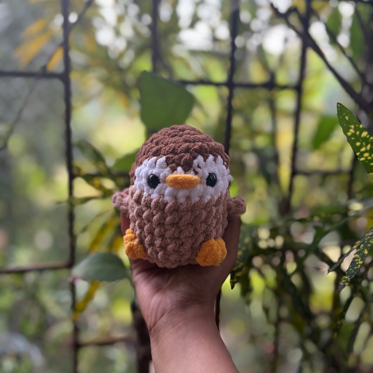Hand holding a small crochet penguin toy with a blurred natural background