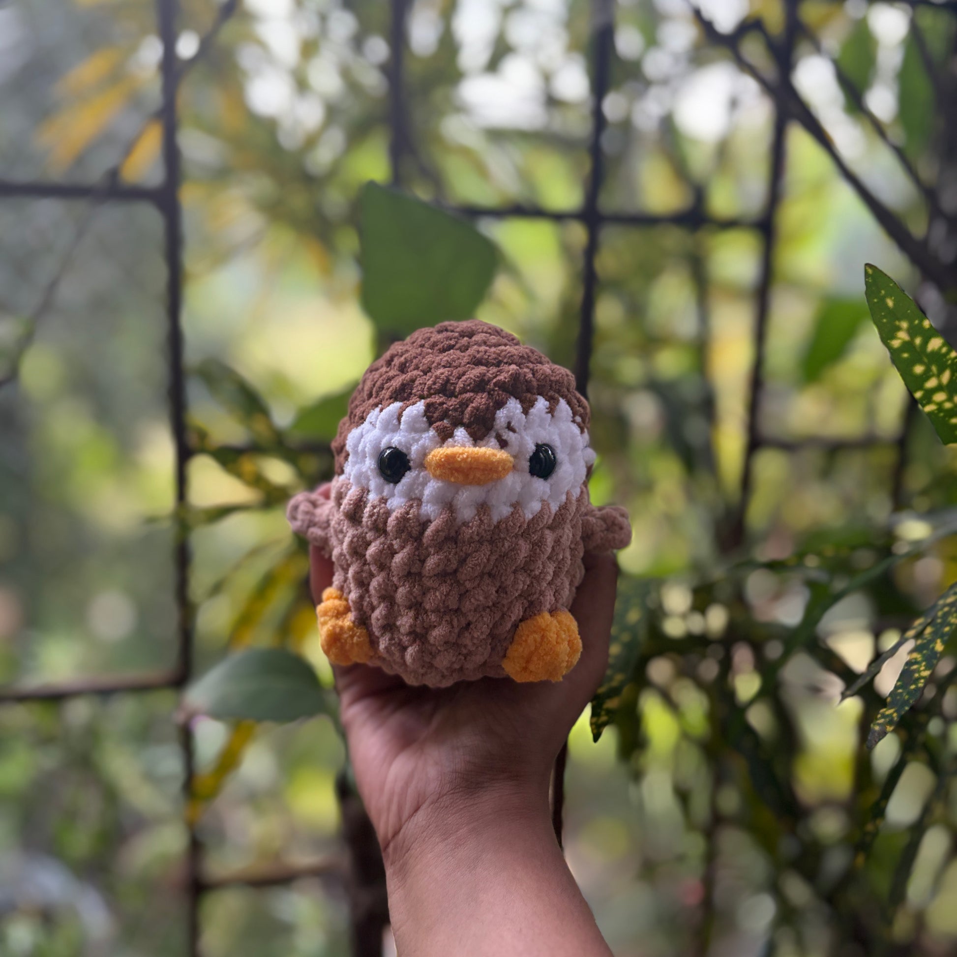 Hand holding a small crochet penguin toy with a blurred natural background