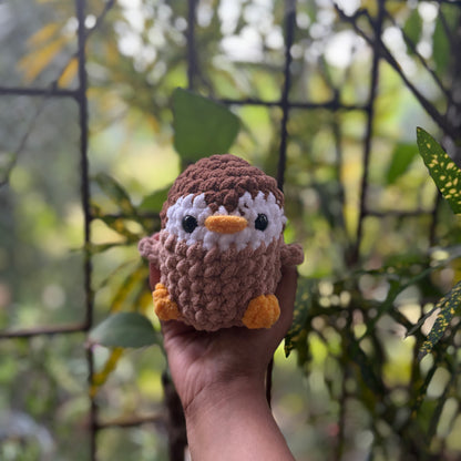 Hand holding a small crochet penguin toy with a blurred natural background