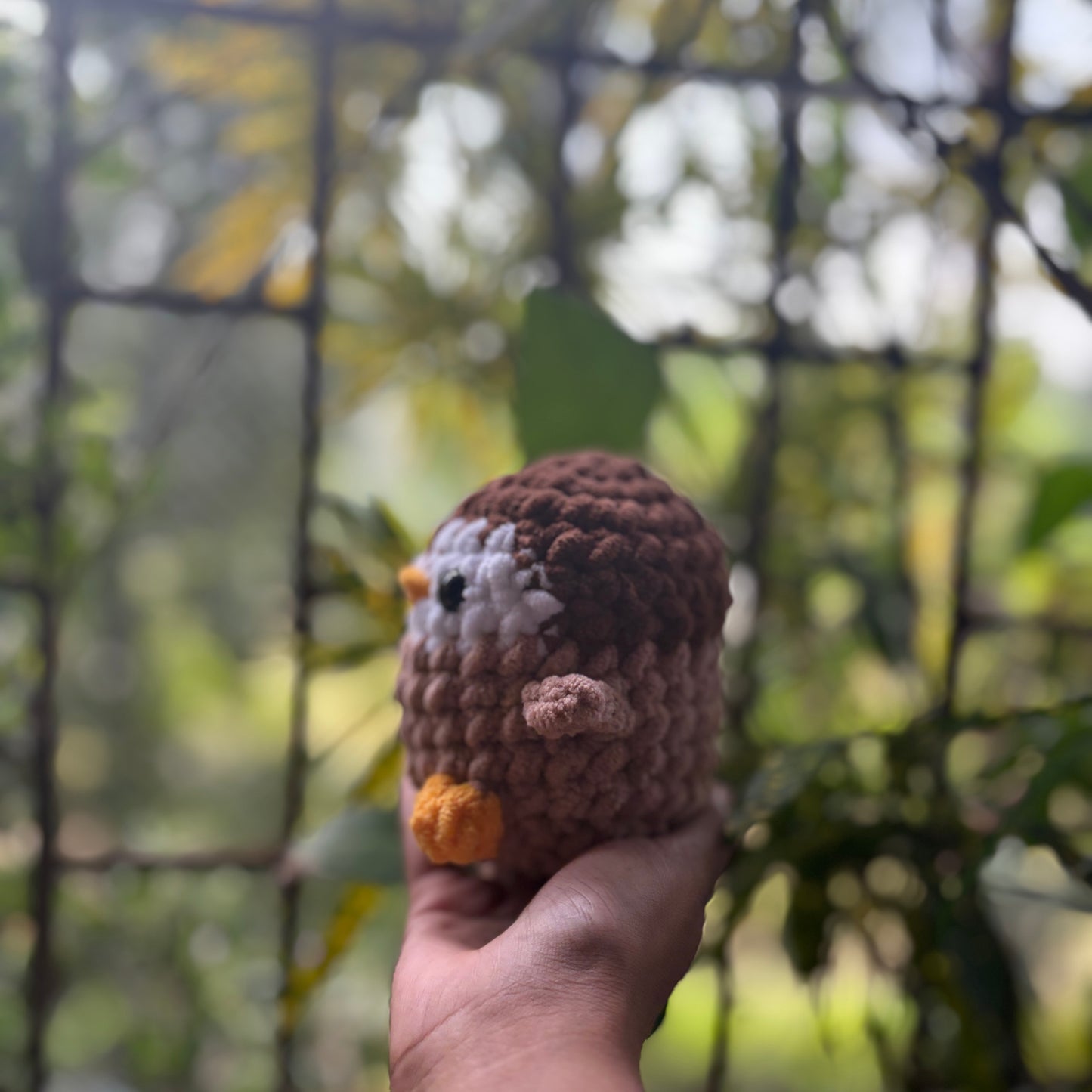 Hand holding a small crochet penguin toy with a blurred natural background