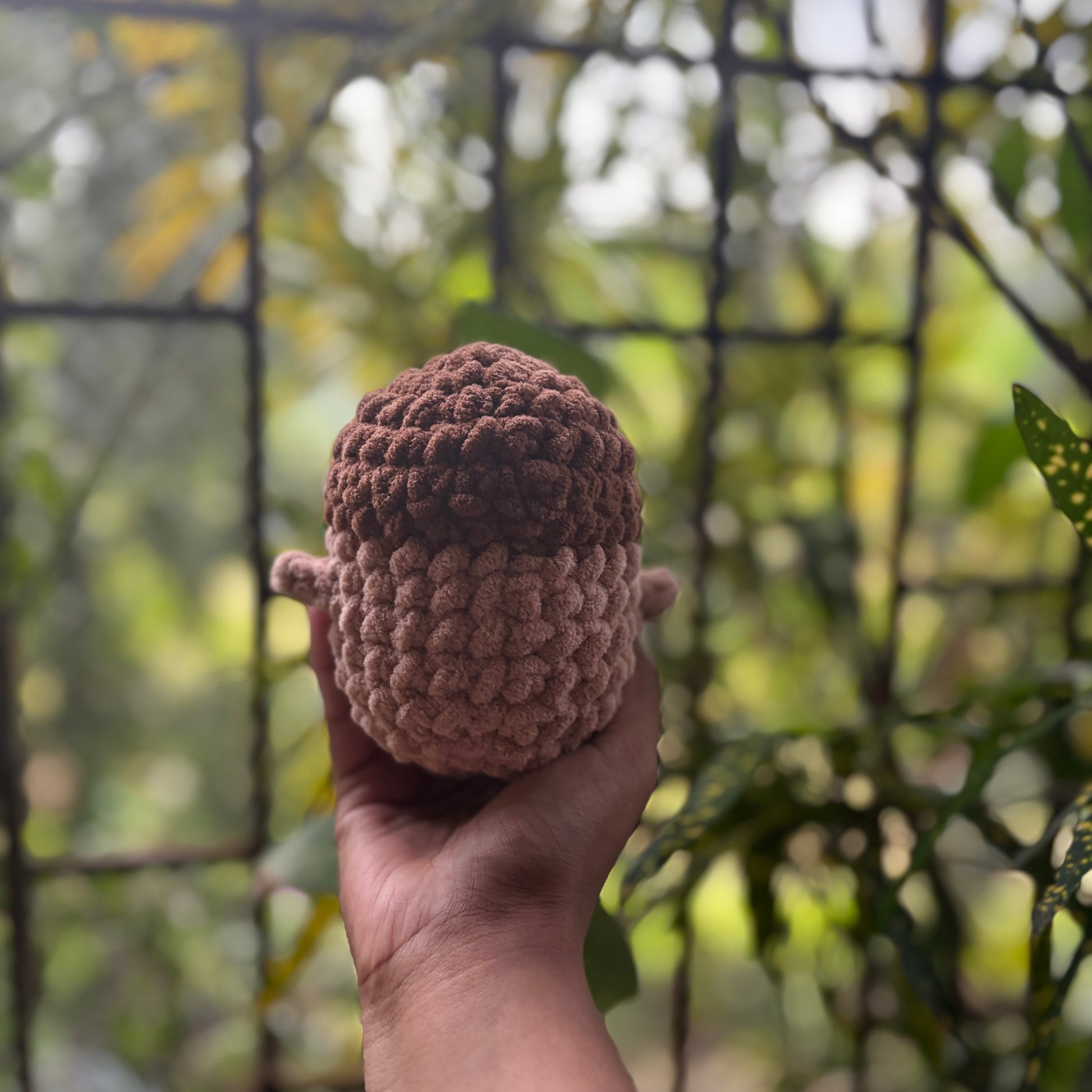 Hand holding back of a small crochet penguin toy with a blurred natural background