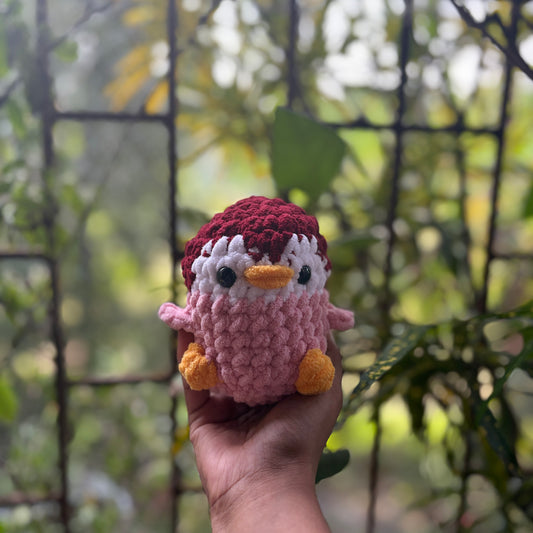 Hand holding a small crochet penguin toy with a blurred natural background