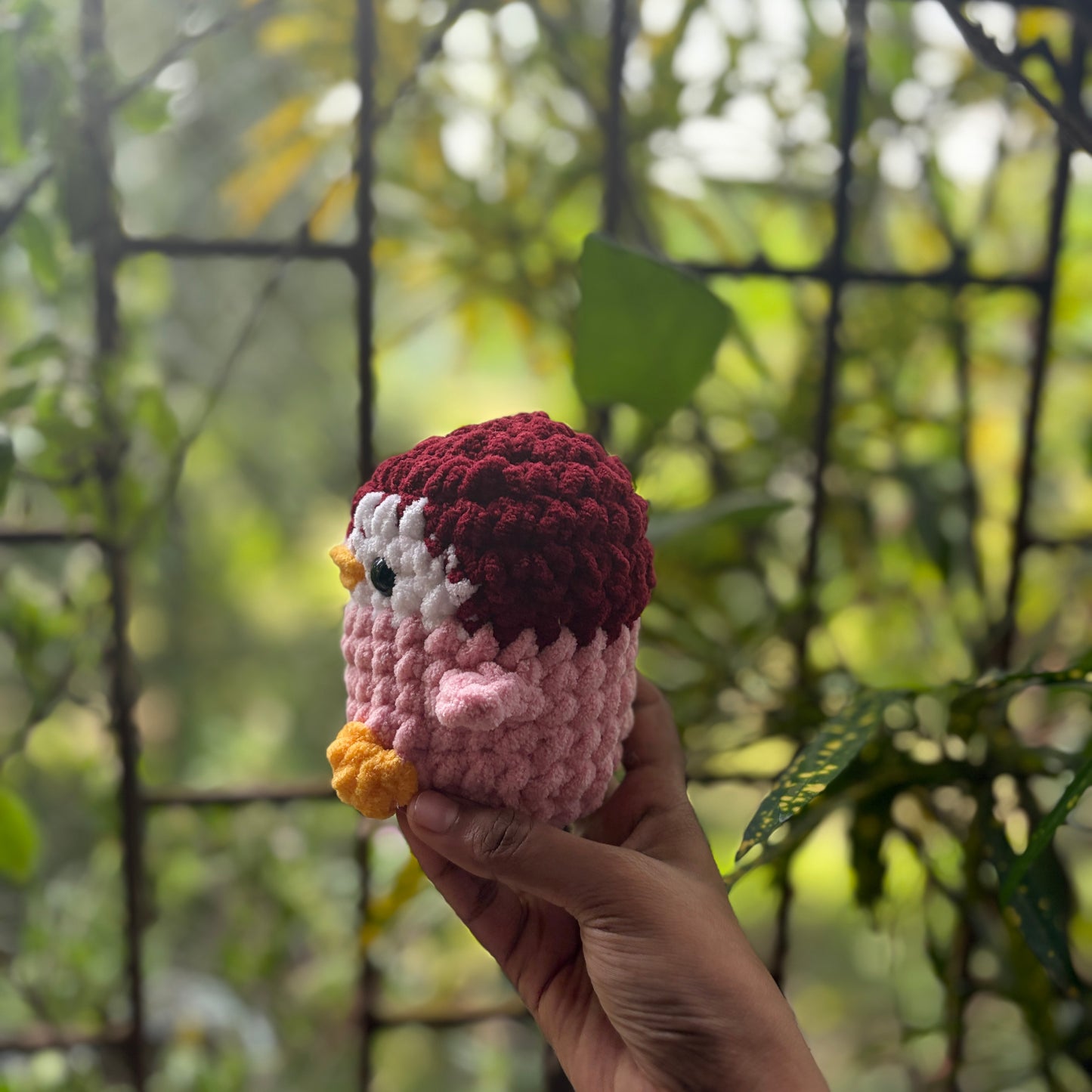 Hand holding a small crochet penguin toy with a blurred natural background