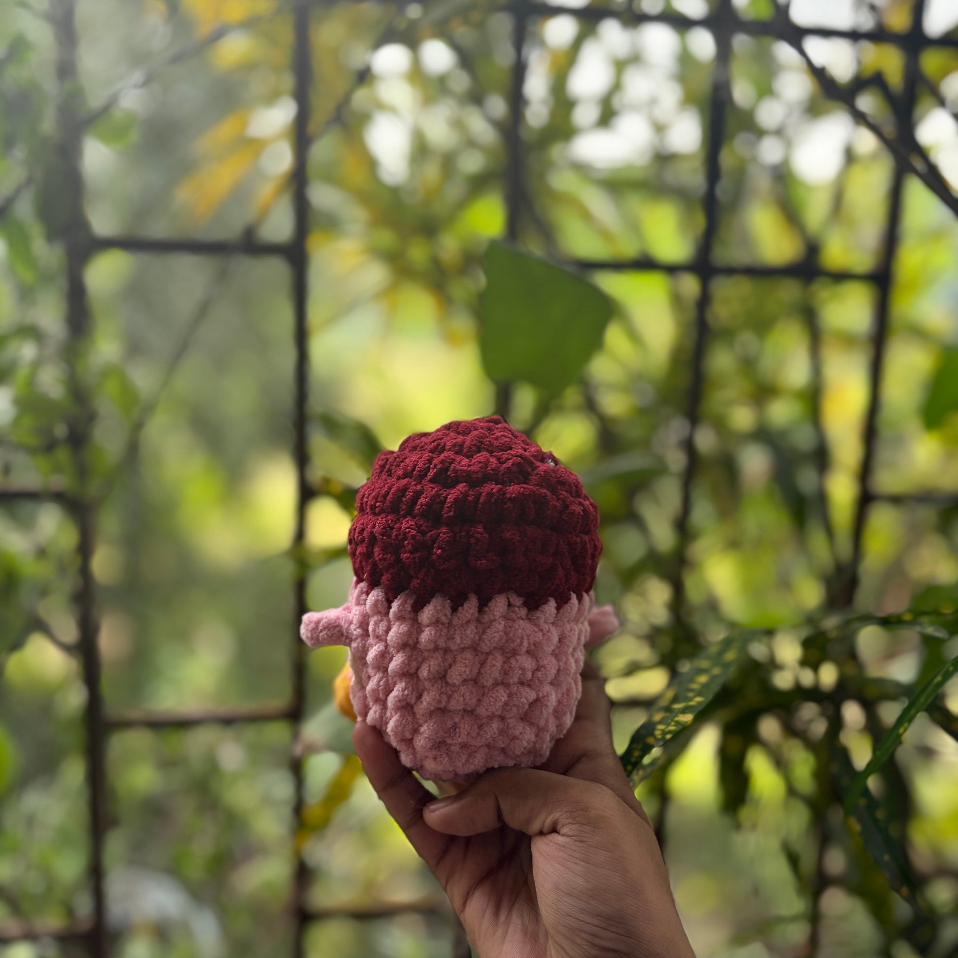 Hand holding back of a small crochet penguin toy with a blurred natural background